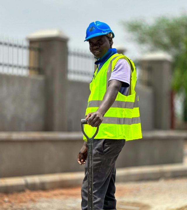 Outdoor scene of a construction worker with safety gear and shovel on a site.